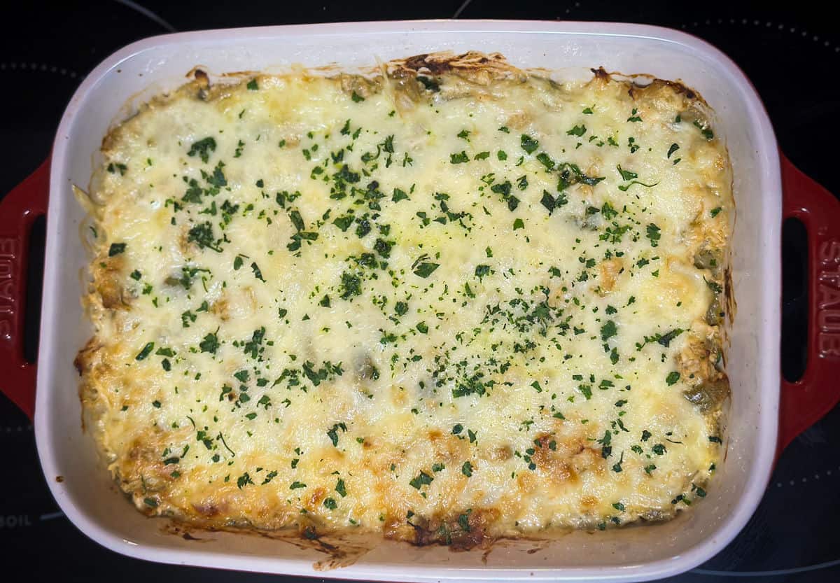 a photo of green chile chicken casserole after baking with cheese melted and garnished with minced cilantro in a white and red casserole.