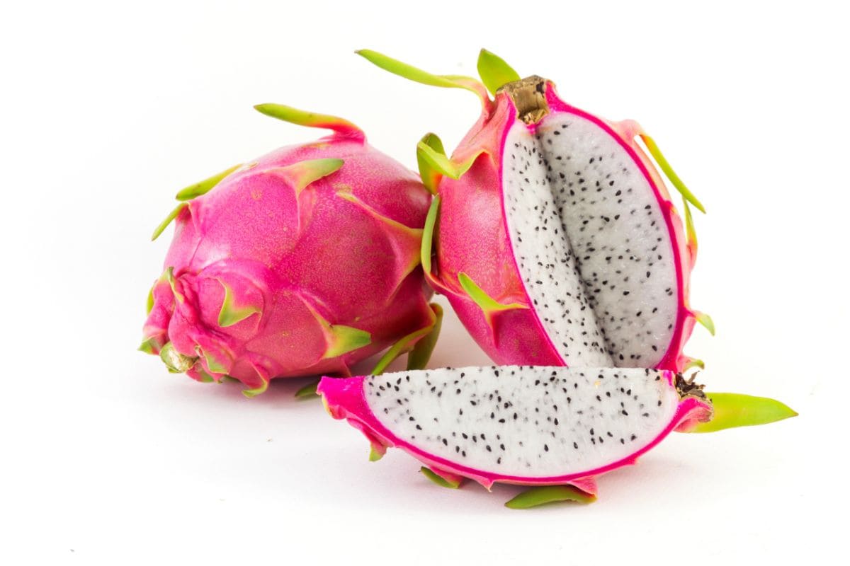 A bright pink dragon fruit with green spikes and a white flesh with tiny black seeds in it.