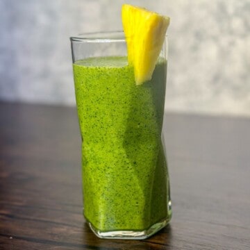 A tall glass of detox island green smoothie with bright green colors and tiny dark green speckles. The glass is garnished with a slim slice of pineapple.