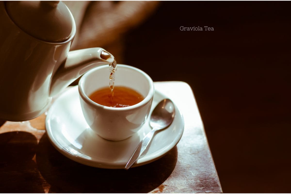 A dark photo of a white tea cup and saucer being filled by a lifted white teak kettle depicting someone's daily routine with graviola tea.