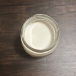 A mason jar filled with creamy cashew milk with a dark wooden backdrop.