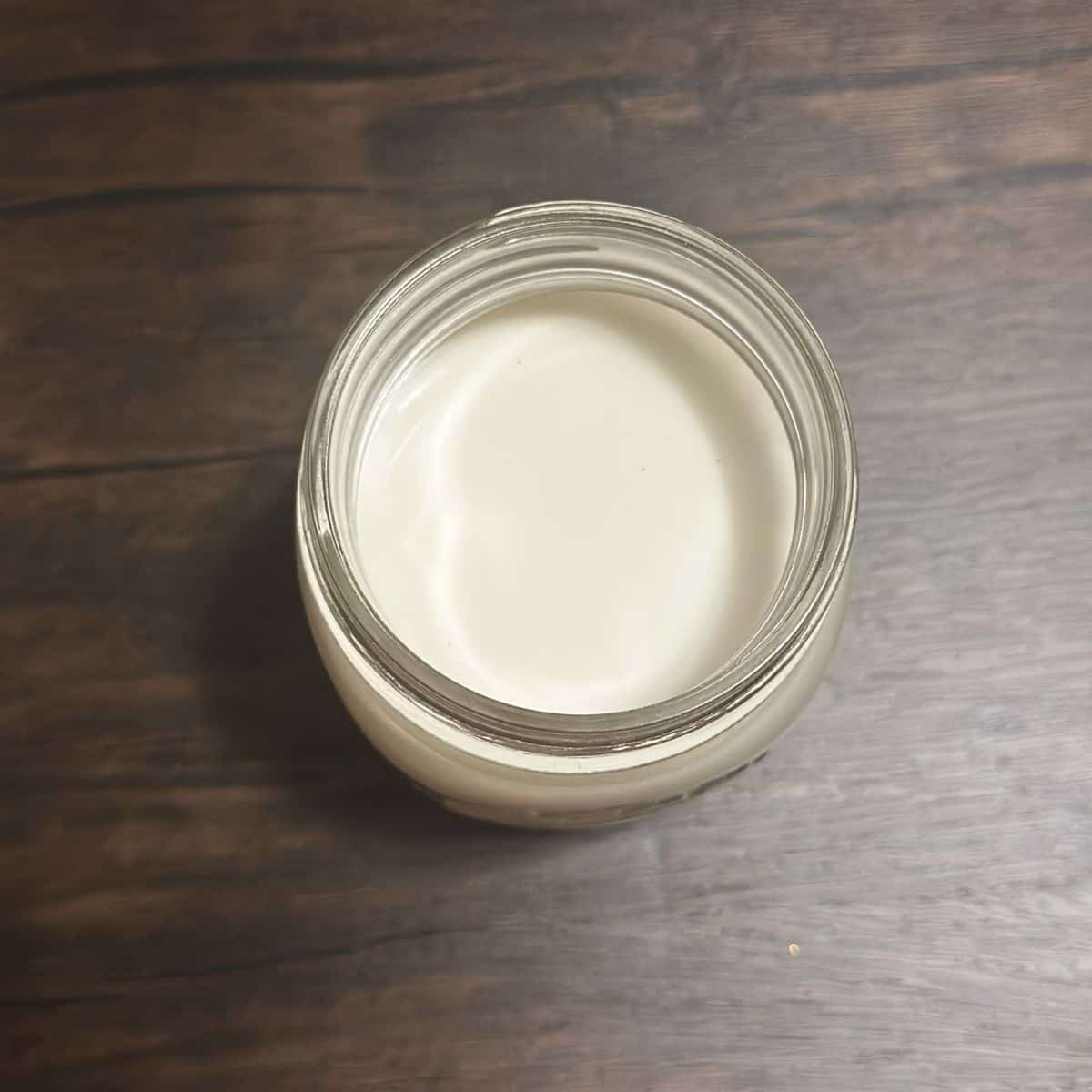 An aerial view of an open mason jar filled with creamy cashew milk with a dark wooden backdrop.