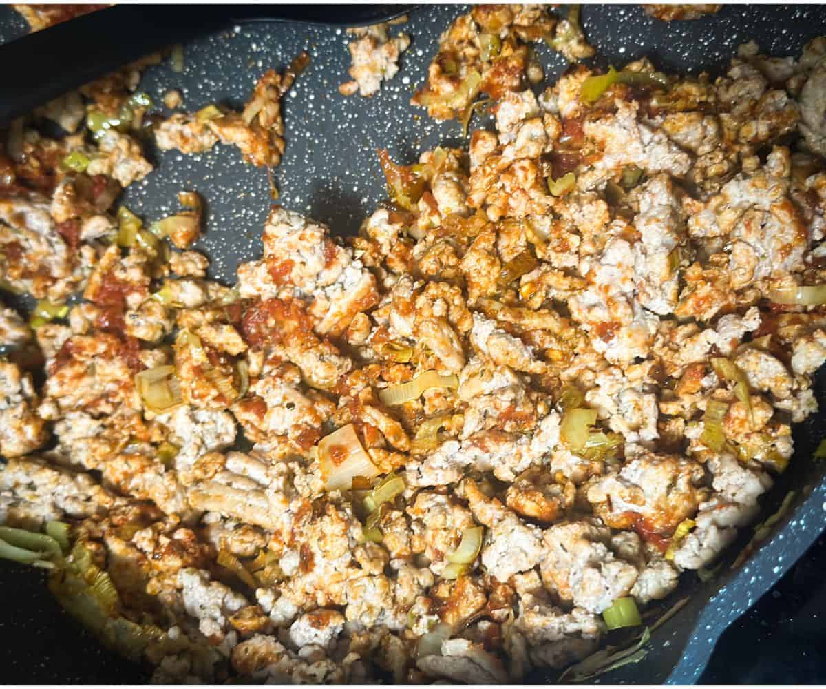 ground turkey cooked and mixed with sauteed leeks and garlic with a touch of tomato paste in a grey skillet.