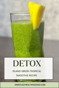 A photo of a tall glass of detox island green smoothie with bright green colors and tiny dark green speckles. The glass is garnished with a slim slice of pineapple. A white box laminated over the drink has text that says detox in large letters and in smaller letters it says island green tropical smoothie recipe mindfullyhealthyliving.com