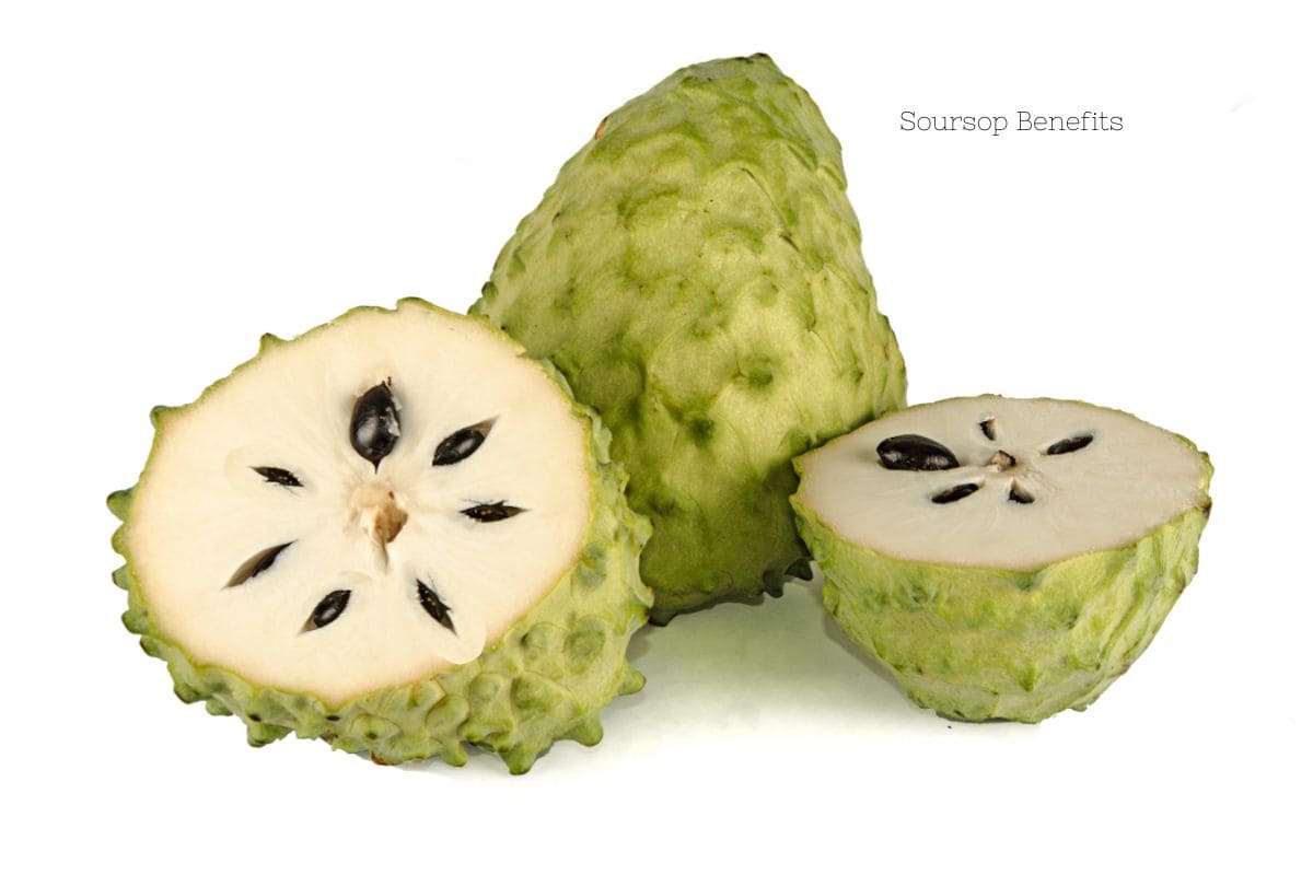A green scaly fruit named soursop is cut in half to reveal a white flesh and a star pattern of black oblong seeds.
