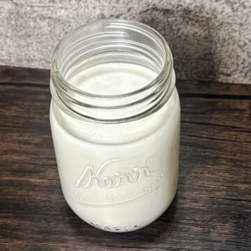 A mason jar filled with creamy cashew milk that shows the front of the clear jar as well as slightly some of the top of the jar.