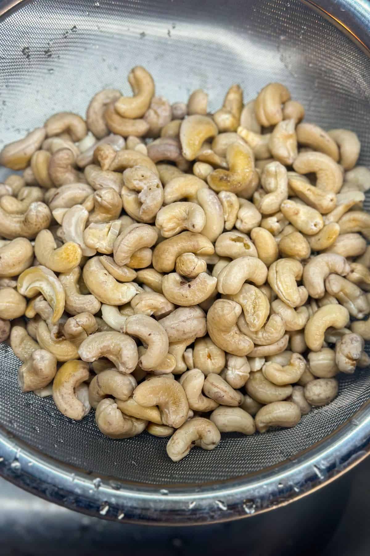 A metal mesh strainer filled with just rinsed and soaked raw cashew nuts.