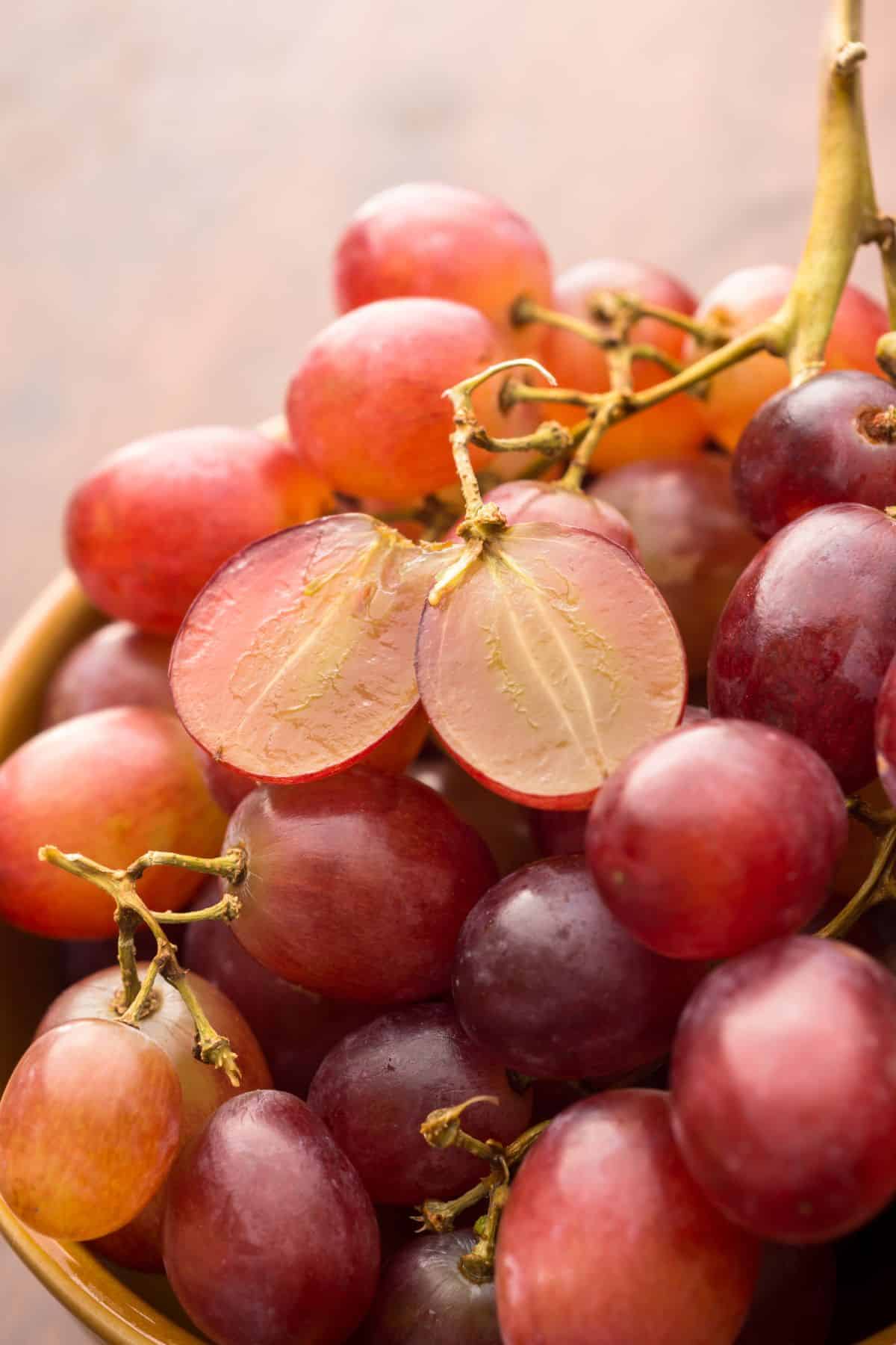 a pile of red grapes with one or two cut open to reveal seedless grapes.