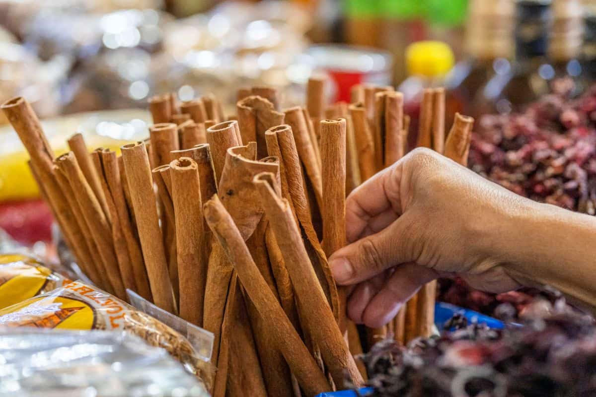 A person shopping for a cinnamon stick in a market. Cinnamon sticks are lined up among other whole and packaged spices in a street market seting.