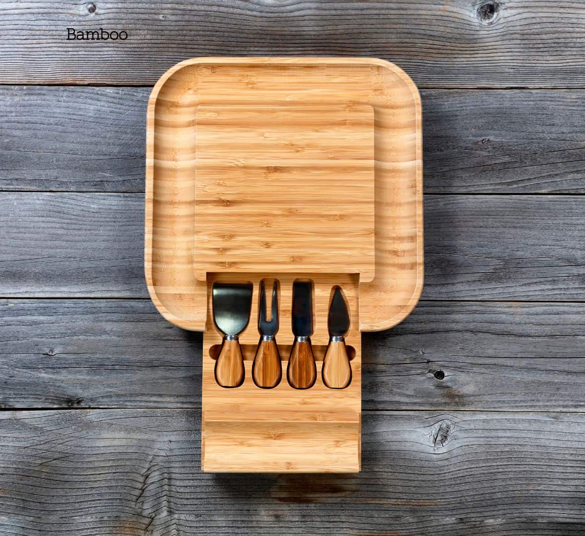 A set of eco-friendly bamboo cheese knives neatly arranged on a matching bamboo cutting board, set against a rustic gray wooden background.