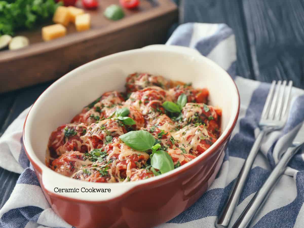 A delicious baked pasta dish with melted cheese and fresh basil in a red ceramic baking dish, showcasing the beauty and safety of using non-toxic ceramic cookware for healthy home cooking.