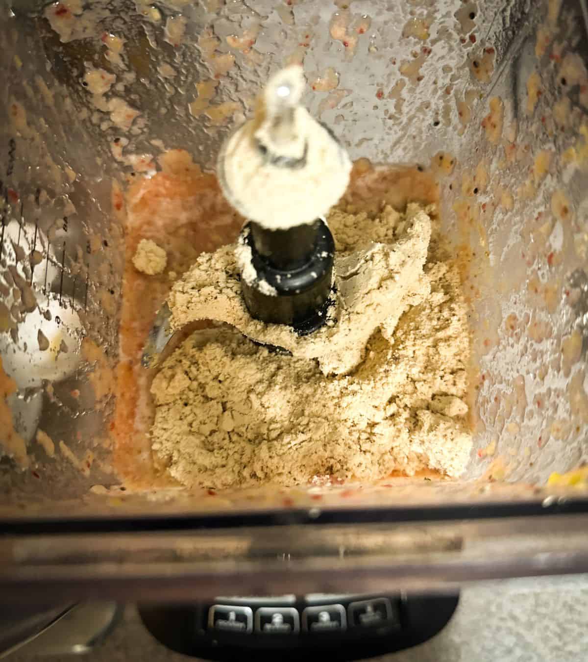 An aerial view of the inside of a a blender that has smoothie partially blended and protein powder scooped on top, ready to continue blending.