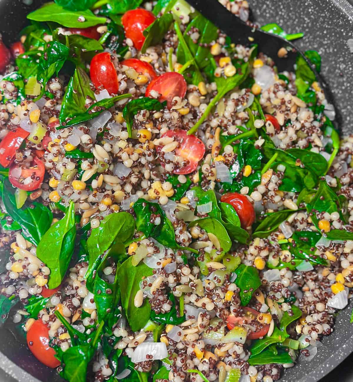 Trader Joe's Harvest Blend grains being mixed with fresh spinach leaves and halved cherry tomatoes in a pan