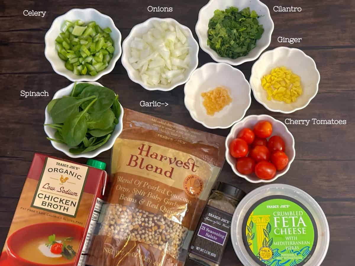 Labeled ingredients for the recipe laid out on a wooden surface, including celery, onions, cilantro, ginger, spinach, garlic, cherry tomatoes, and packages of Trader Joe's products.