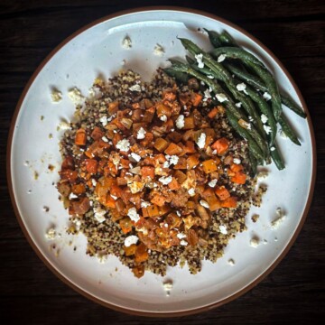 A plate with a serving of quinoa, topped with a holiday hash of sweet potatoes and sausage, garnished with feta cheese and green beans on the side.