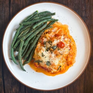 A beautifully plated serving of Trader Joe's Chicken Meatball Spaghetti Bake, accompanied by a side of seasoned green beans, presented on a white plate against a dark wood background, highlighting the dish's appetizing colors and textures.