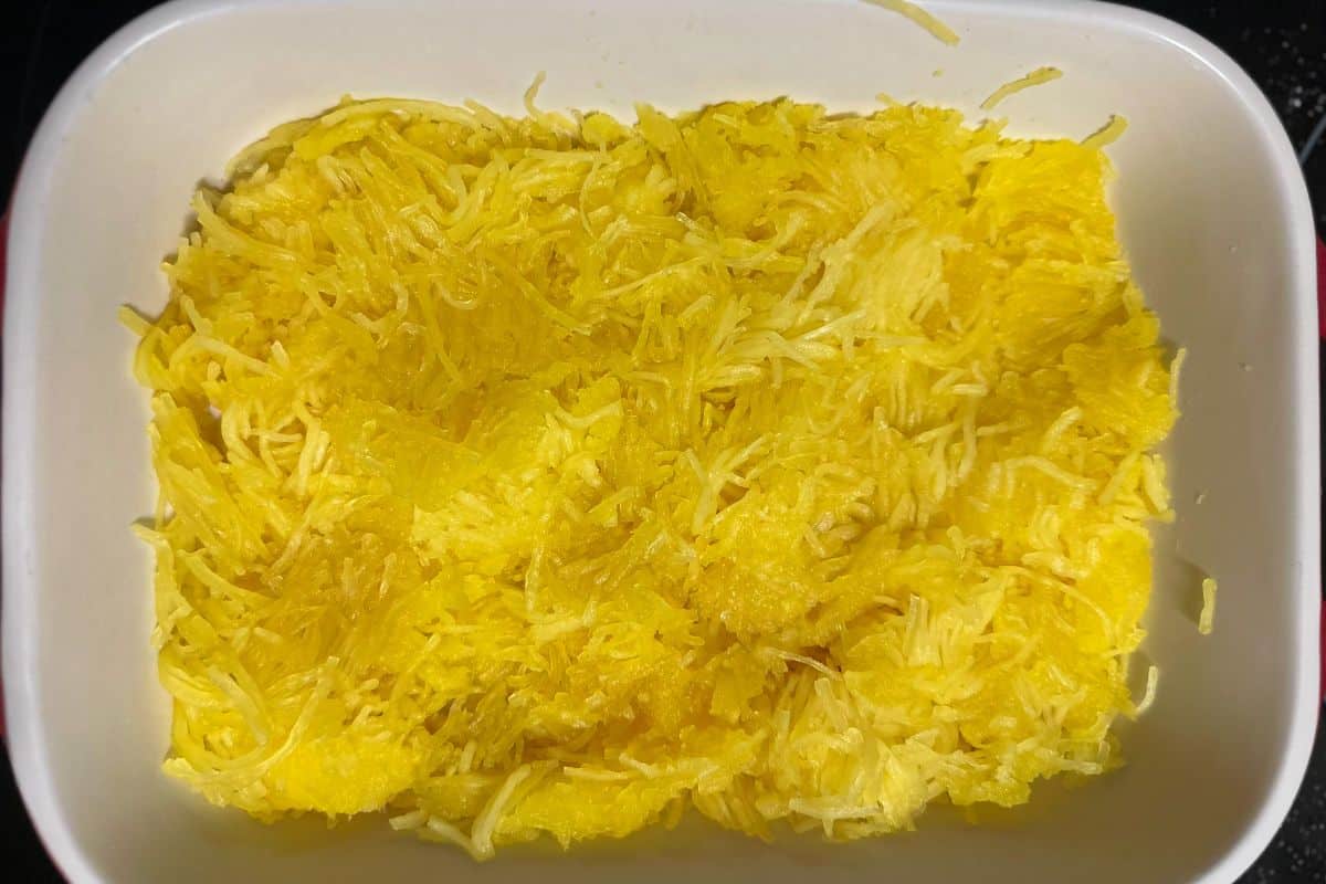 A white casserole dish filled with bright yellow spaghetti squash strands as the first layer for the spaghetti bake.