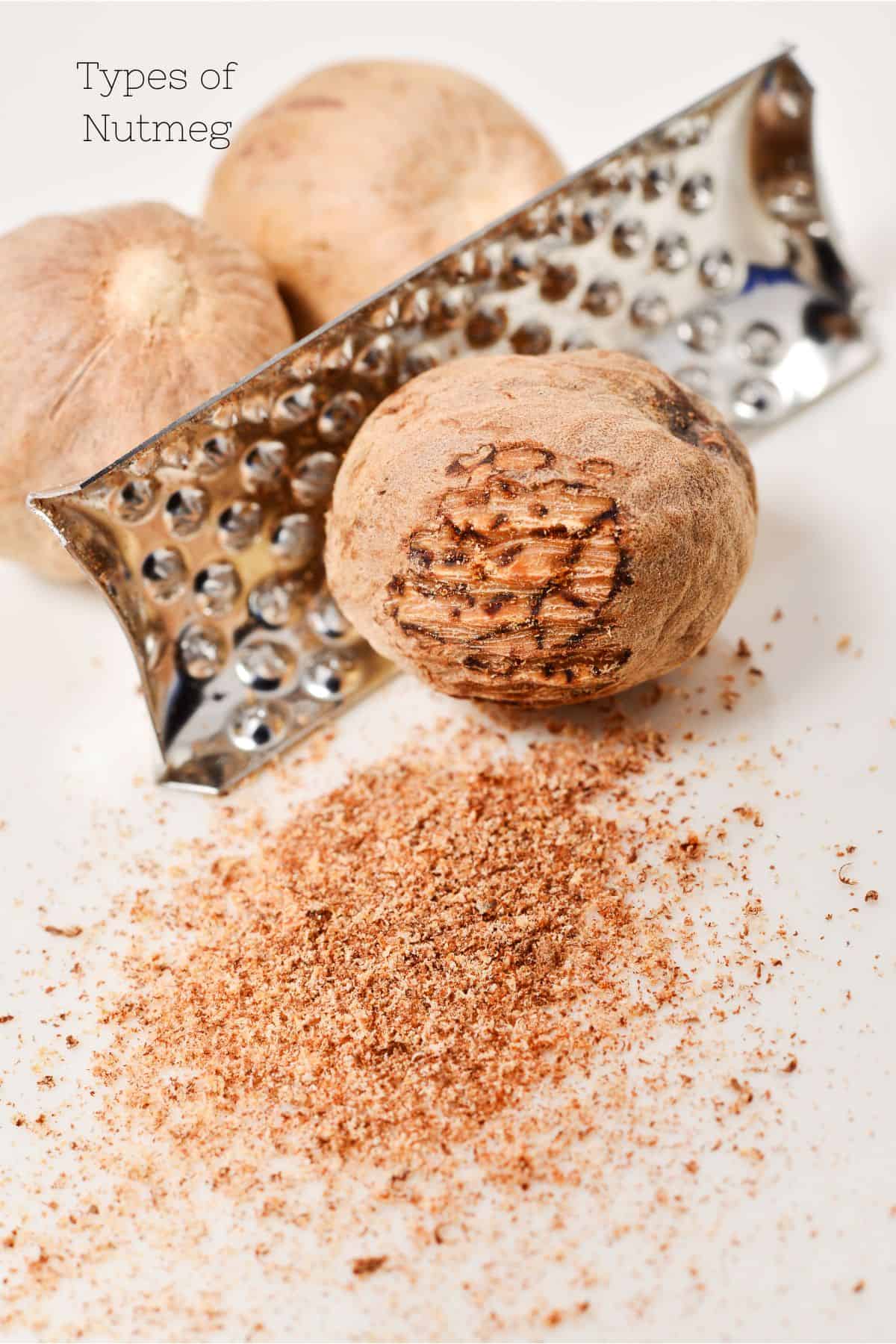 Different types of whole nutmeg next to a grater with freshly grated nutmeg on the side.