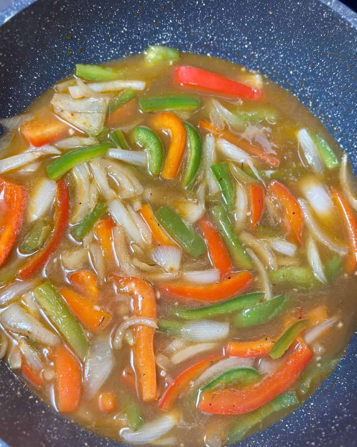 Colorful sliced onions and bell peppers simmering in rich bone broth for Southern Cajun Smothered Chicken.
