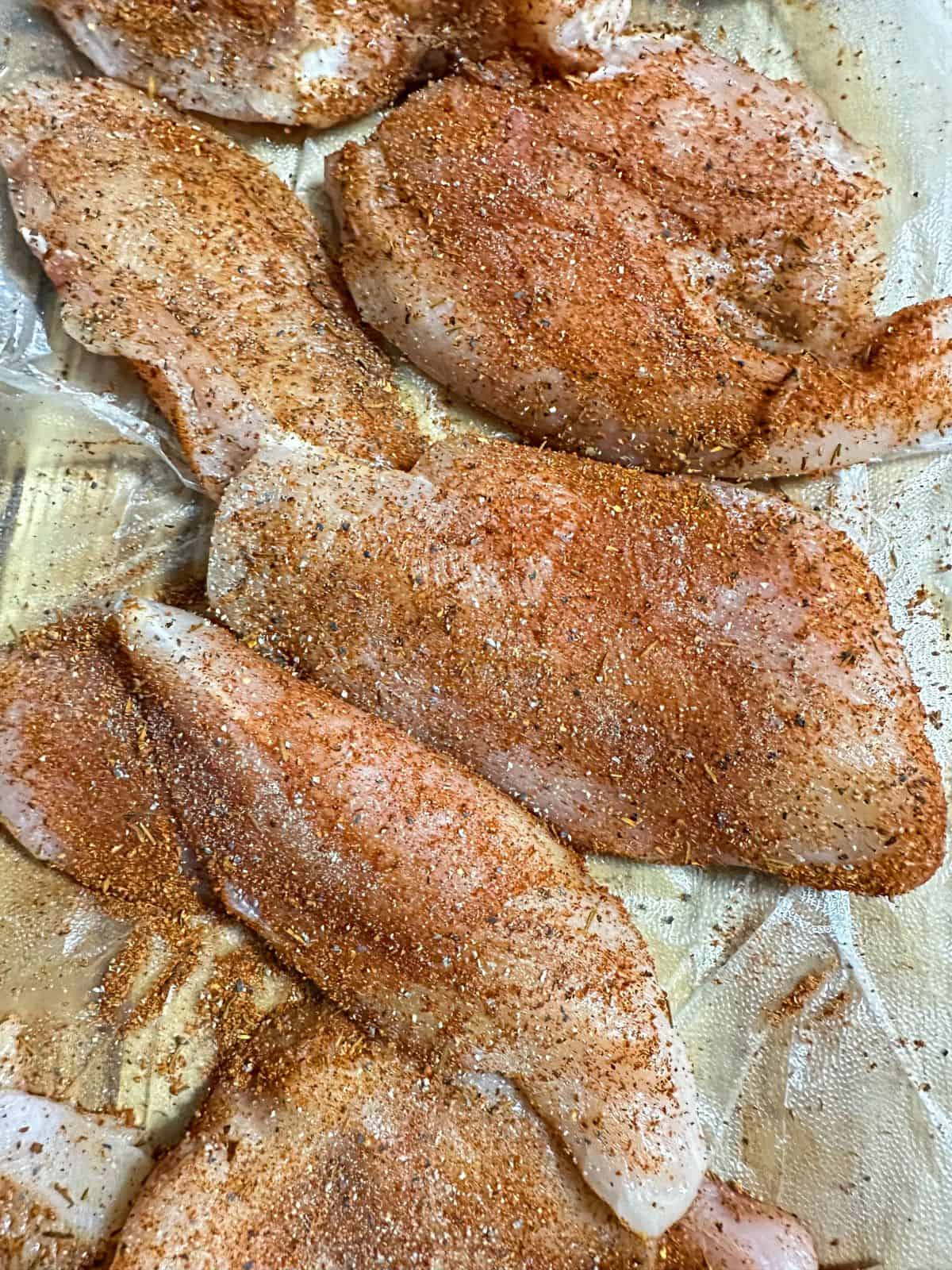 Raw chicken breasts liberally seasoned with Cajun spices, prepped for browning in the Southern Smothered Chicken recipe.