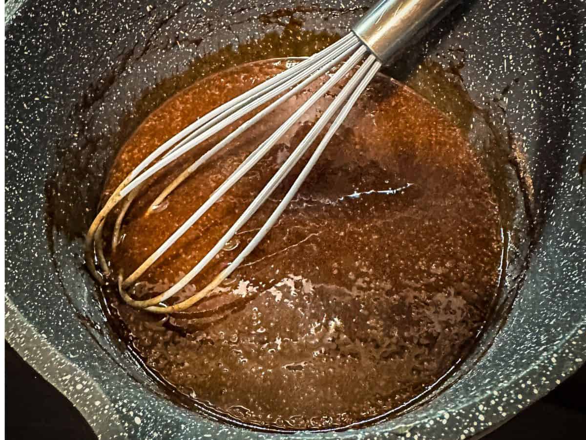 A whisk mixing brown sauce in a pot, preparing the spiced base for peach cobbler.