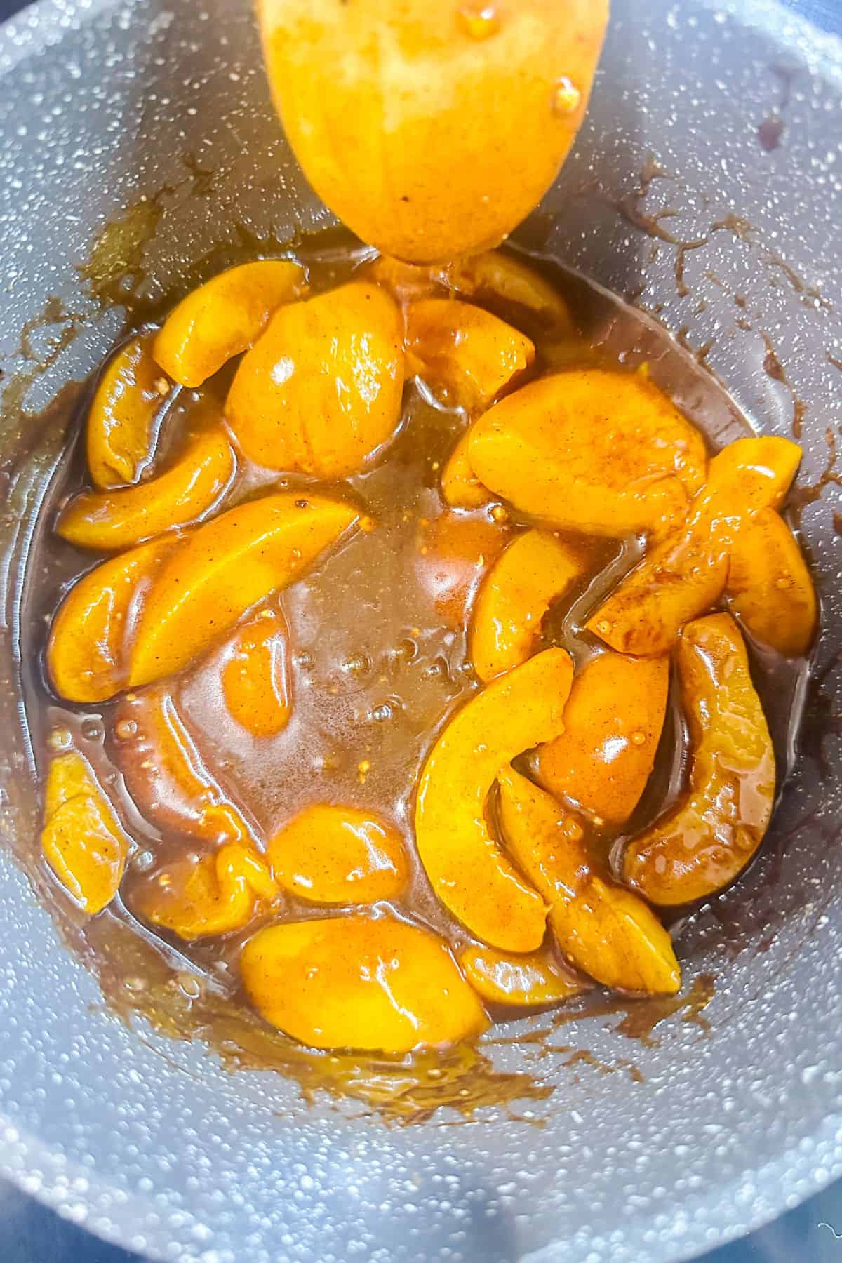 Bright, sliced peaches in a saucepan coated with a glossy, cinnamon-infused sauce