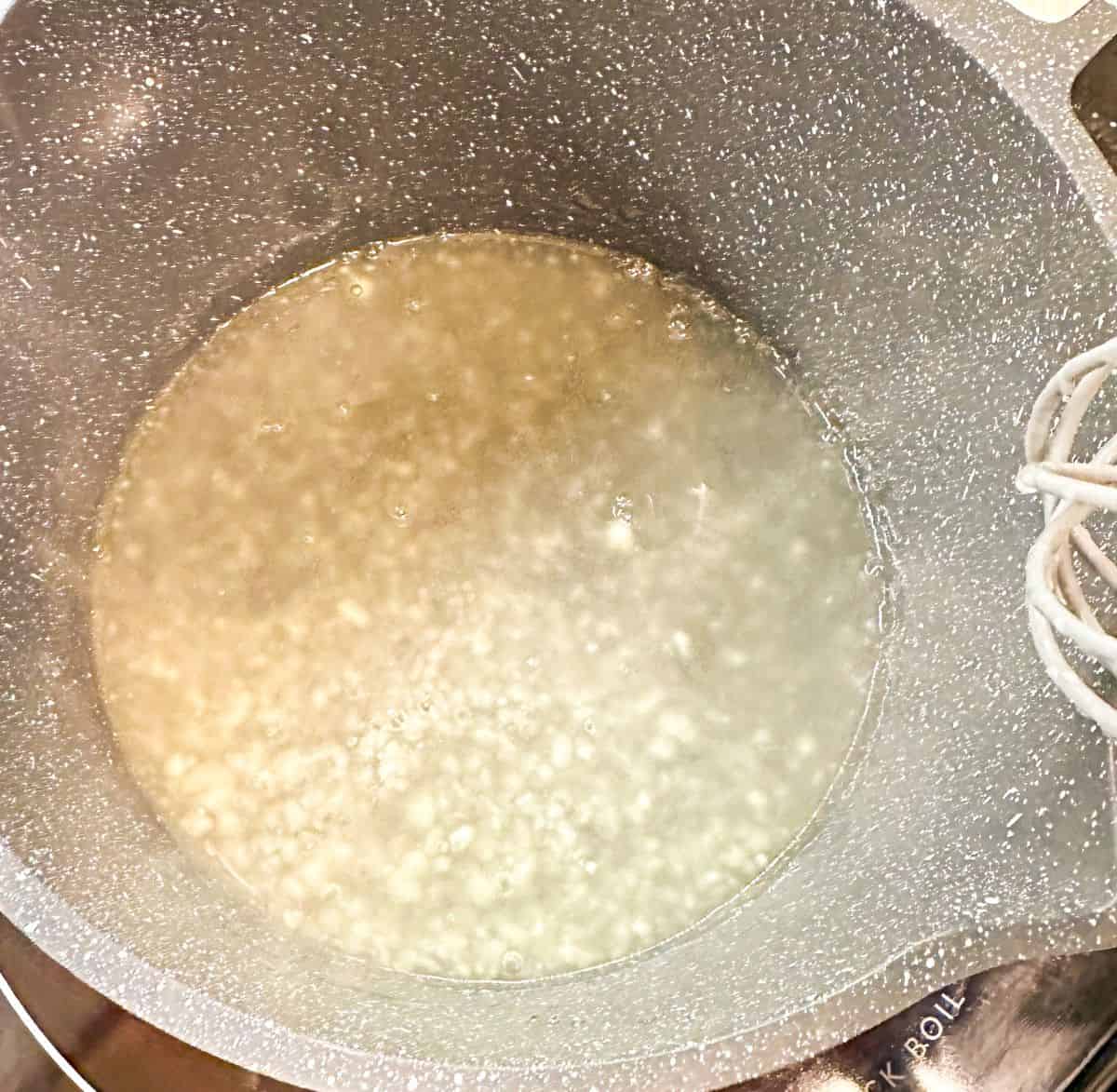 Boiling peach juice in a saucepan being thickened with cornstarch for peach cobbler, with a whisk in view for stirring.