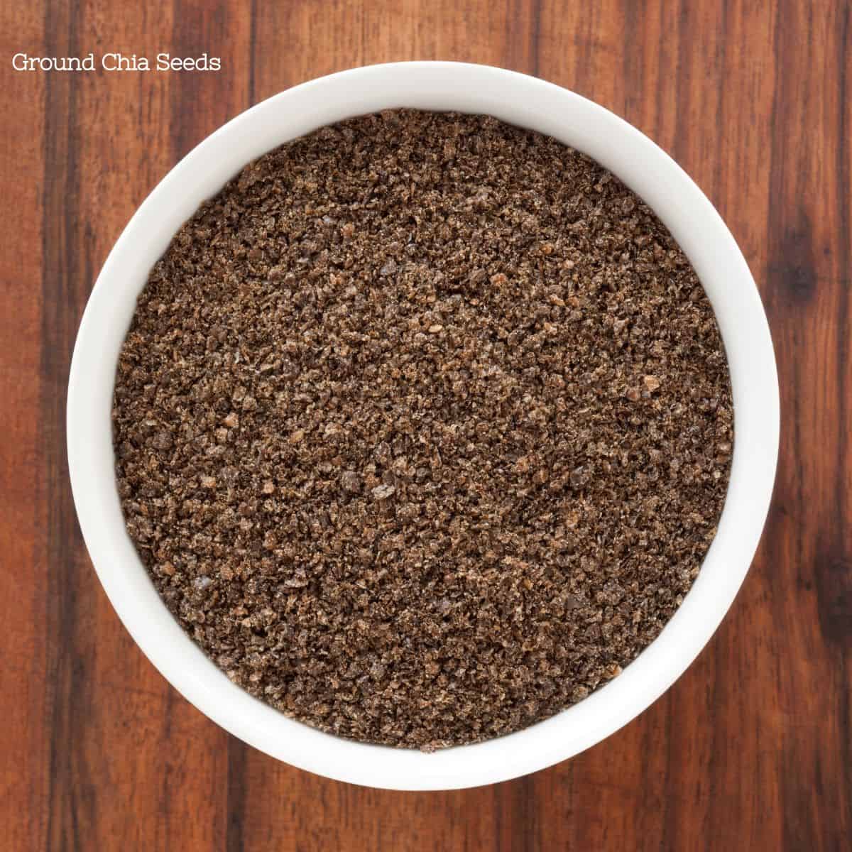 Close-up view of ground chia seeds in a white bowl on a wooden surface