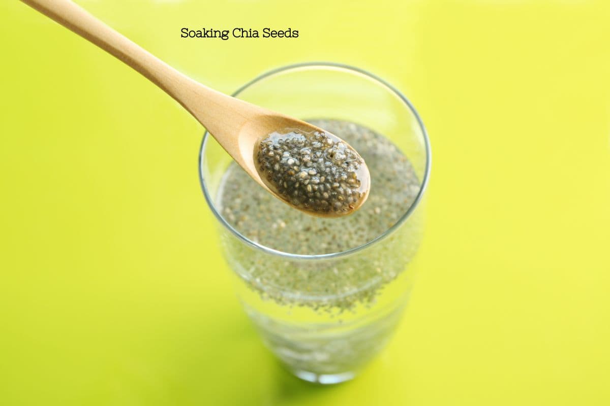 Spoon lifting soaked chia seeds from a glass, showing their gel-like consistency against a yellow background.