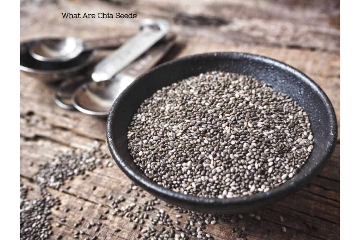 A skillet filled with dry chia seeds with measuring spoons, placed on a rustic wooden table.