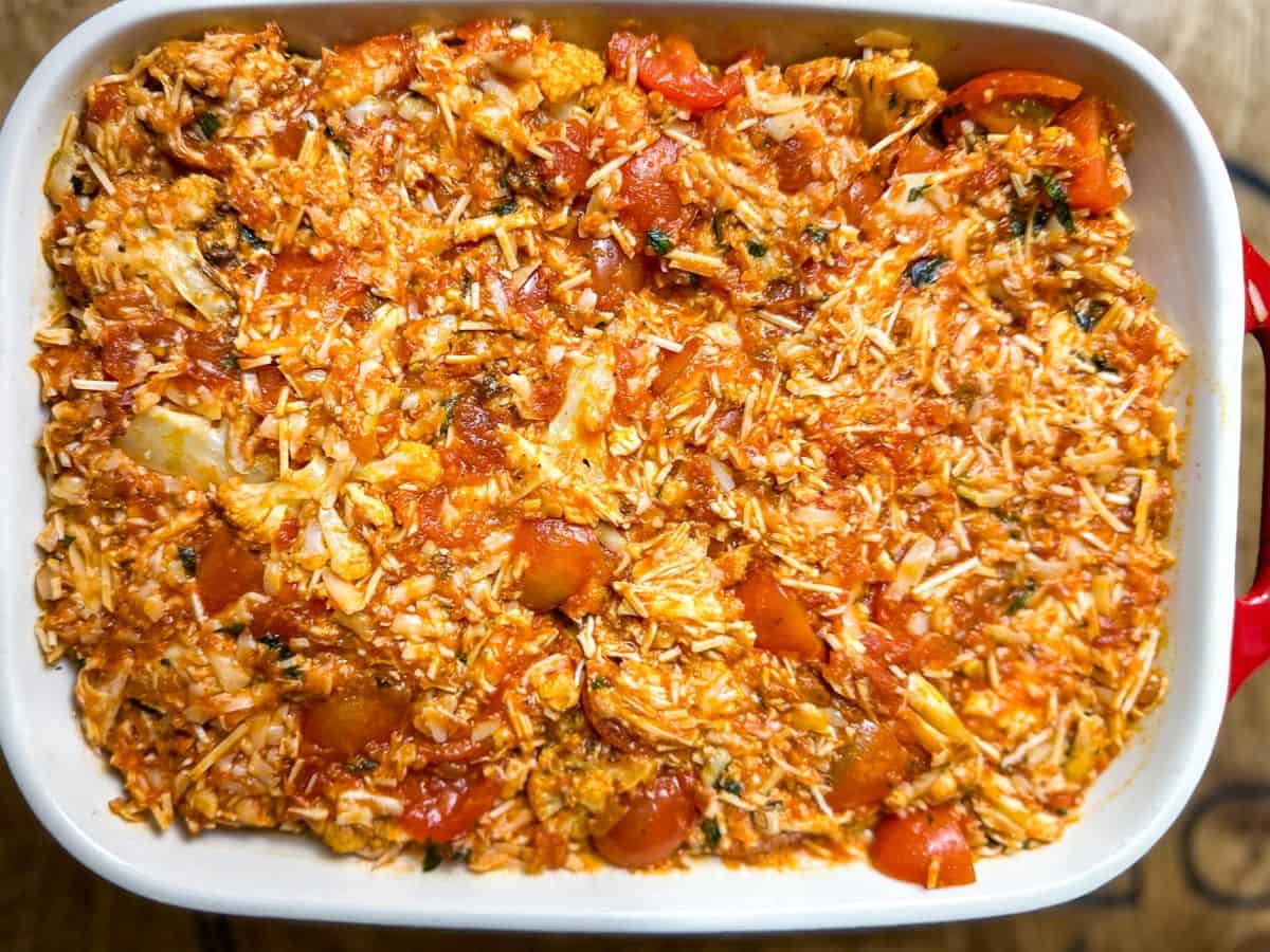 A colorful array of ingredients including shredded chicken, cherry tomatoes, and fresh basil in a glass mixing bowl, ready to be combined for a Keto Chicken Parmesan Casserole