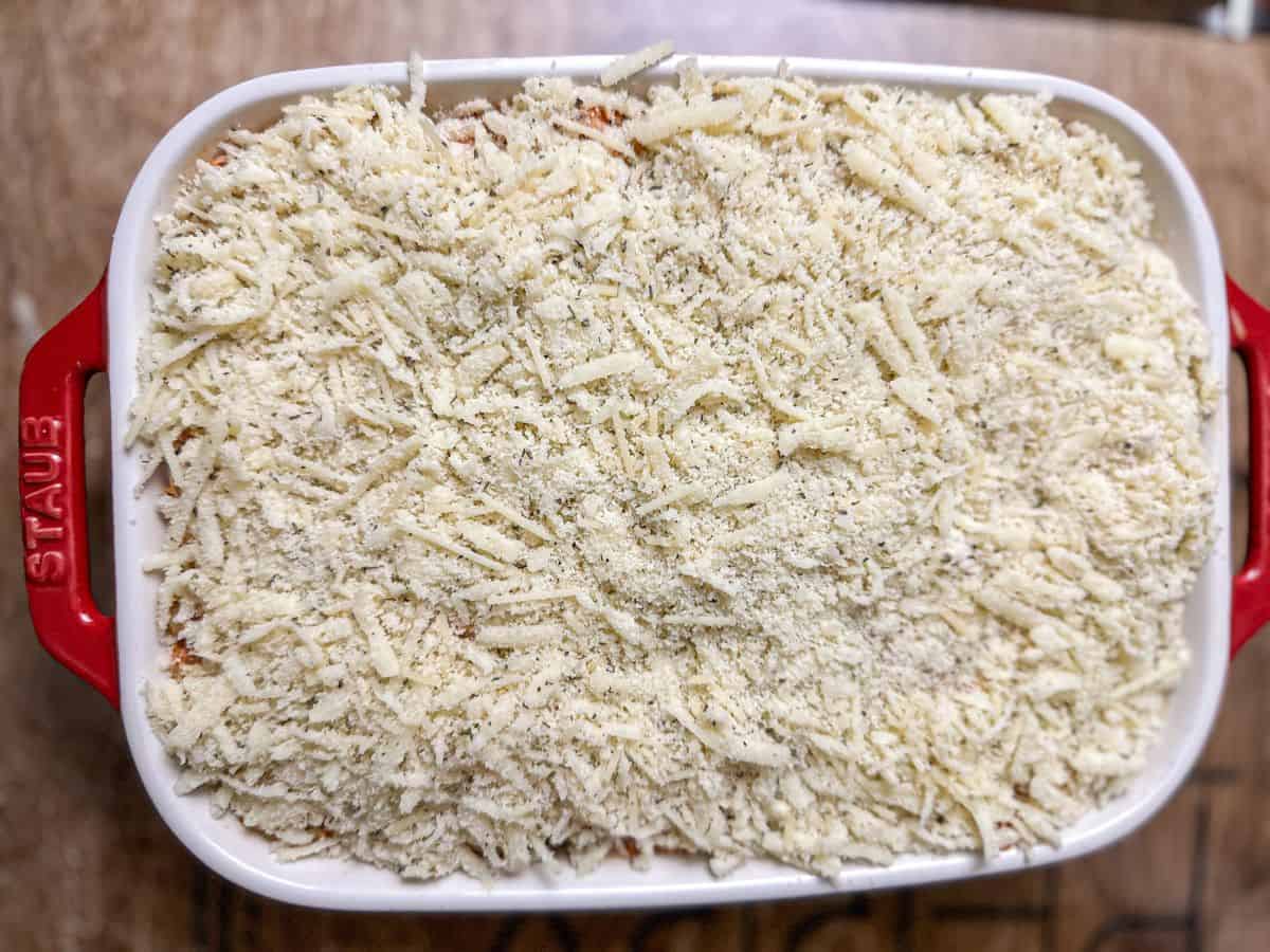 A white casserole dish filled with Keto Chicken Parmesan mixture, topped with a layer of grated Parmesan cheese awaiting its transformation into a golden crust.