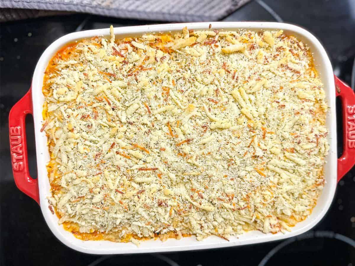 A freshly baked Keto Chicken Parmesan Casserole in a red casserole dish, showcasing a toasted almond flour and Parmesan cheese topping