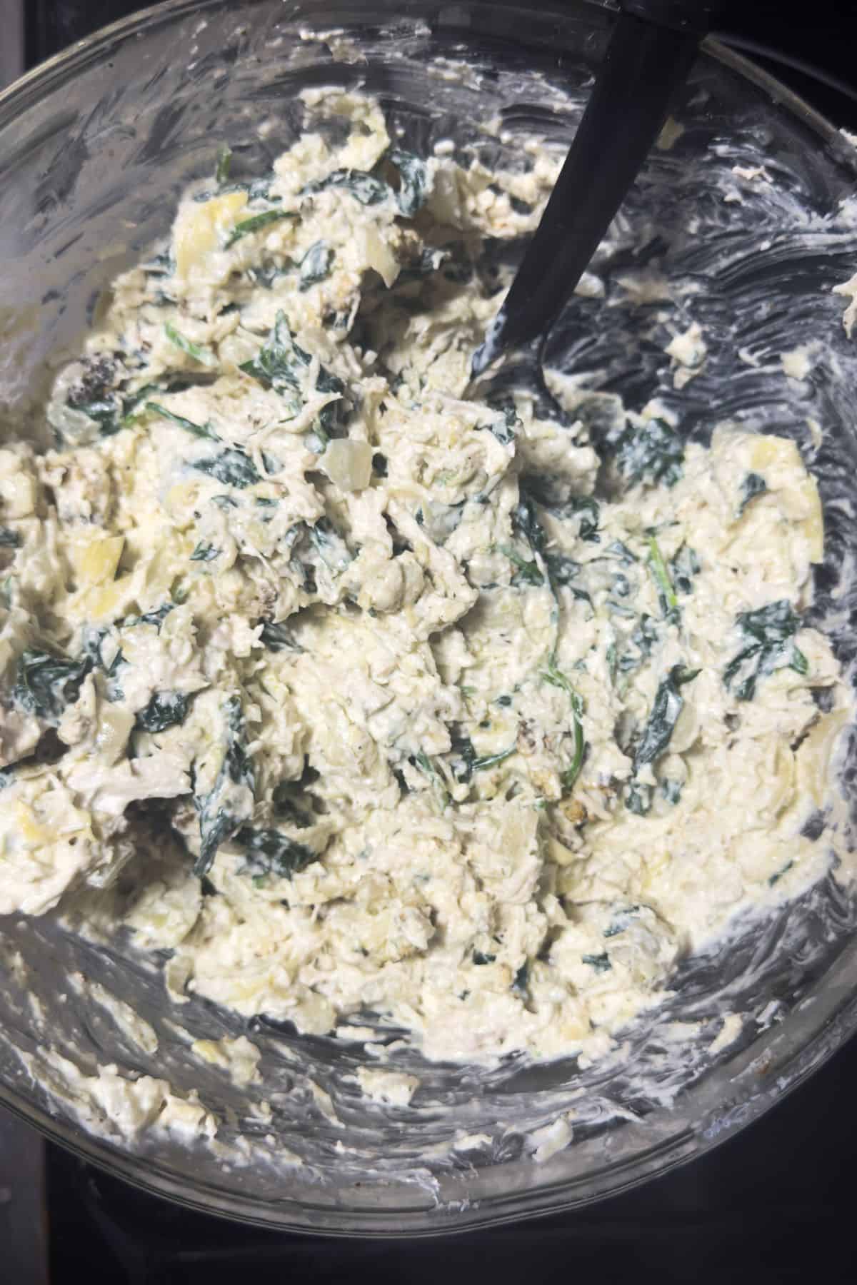A large mixing bowl with the creamy, cheesy spinach and artichoke mixture, ready to be layered into the casserole dish.