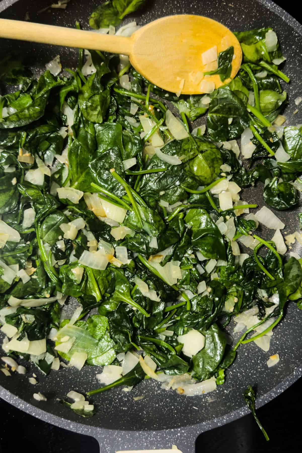 Spinach and onions being sautéed in a skillet for the Keto Spinach Artichoke Chicken Casserole filling.