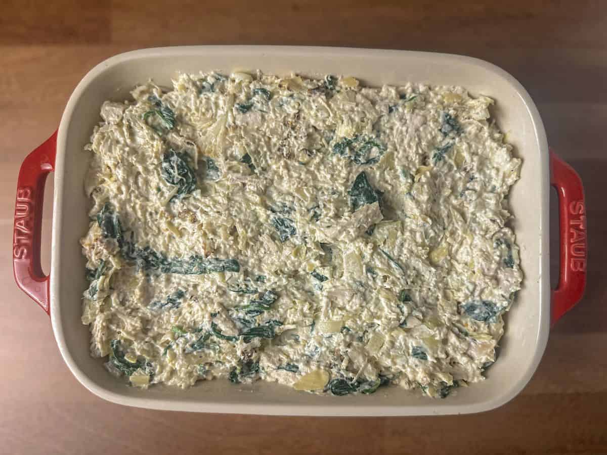 Creamy spinach and artichoke mixture in a white casserole dish ready for topping and baking