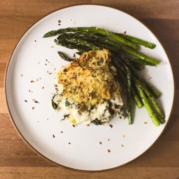 A portion of Keto Spinach Artichoke Chicken Casserole on a plate with asparagus, showcasing the creamy filling.
