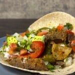 A finished steak fajita on a corn tortilla, generously filled with seasoned meat, peppers, and onions, topped with avocado and a dollop of sour cream.