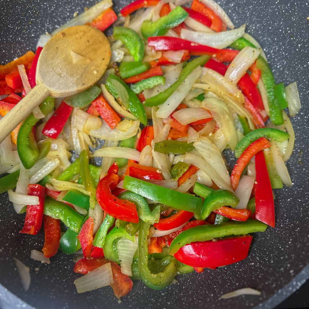 Sautéing sliced green and red bell peppers and onions in a skillet, getting tender and ready for adding to the steak fajitas.
