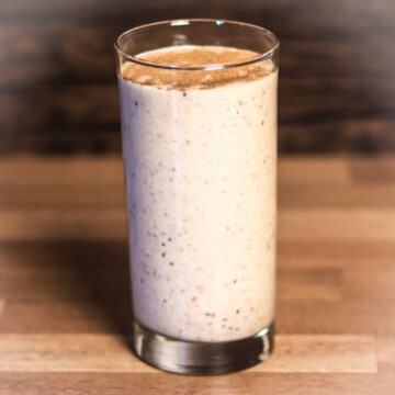 A tall glass of creamy chia banana boost smoothie on a wooden surface, indicative of a nutritious homemade drink