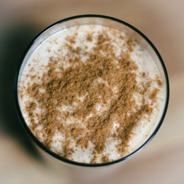 Top view of a freshly blended chia banana smoothie topped with a dusting of cinnamon, in a clear glass on a neutral background.