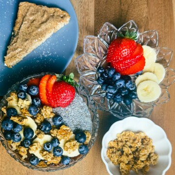 An overhead shot of a fully assembled chia seed pudding dish next to almond butter toast, showcasing the colorful toppings of fresh fruit and granola on the pudding.