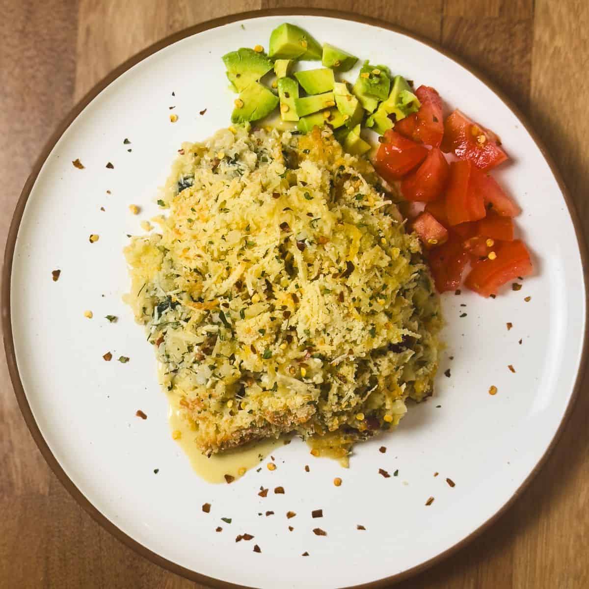Plated serving of keto chicken and cauliflower rice casserole garnished with avocado and tomato