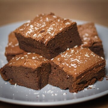 A plate with several square-cut, freshly baked sweet potato protein brownies, lightly sprinkled with desiccated coconut for garnish.