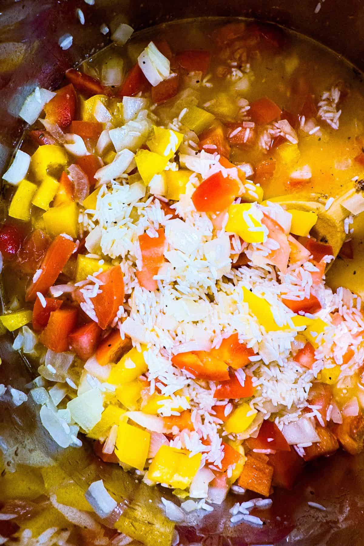 Overhead shot of an Instant Pot with uncooked rice, diced tomatoes, yellow and red bell peppers, and onions, ready to be cooked.