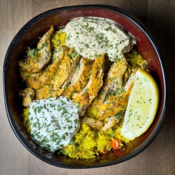 A complete meal in a bowl, featuring sliced Chicken Shawarma on a bed of Saffron Rice, garnished with Tzatziki sauce and lemon wedge.
