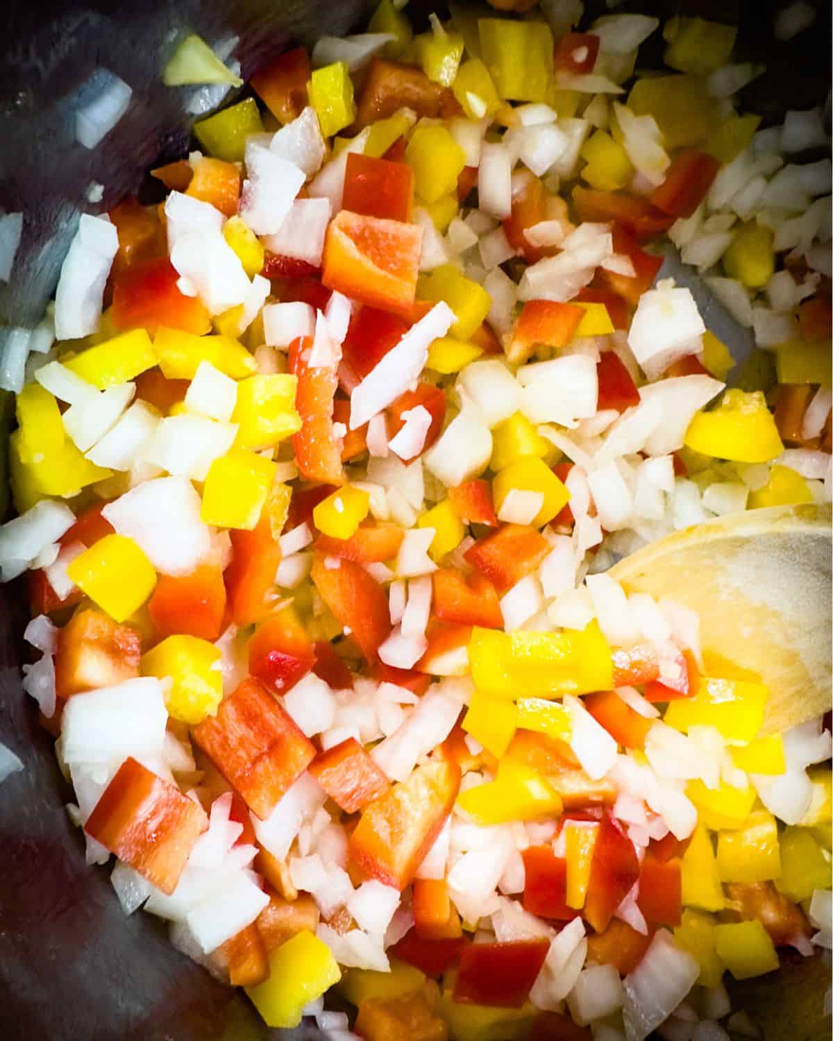 Diced onions, red and yellow bell peppers being sautéed in an Instant Pot, with steam rising, signifying the start of the cooking process.