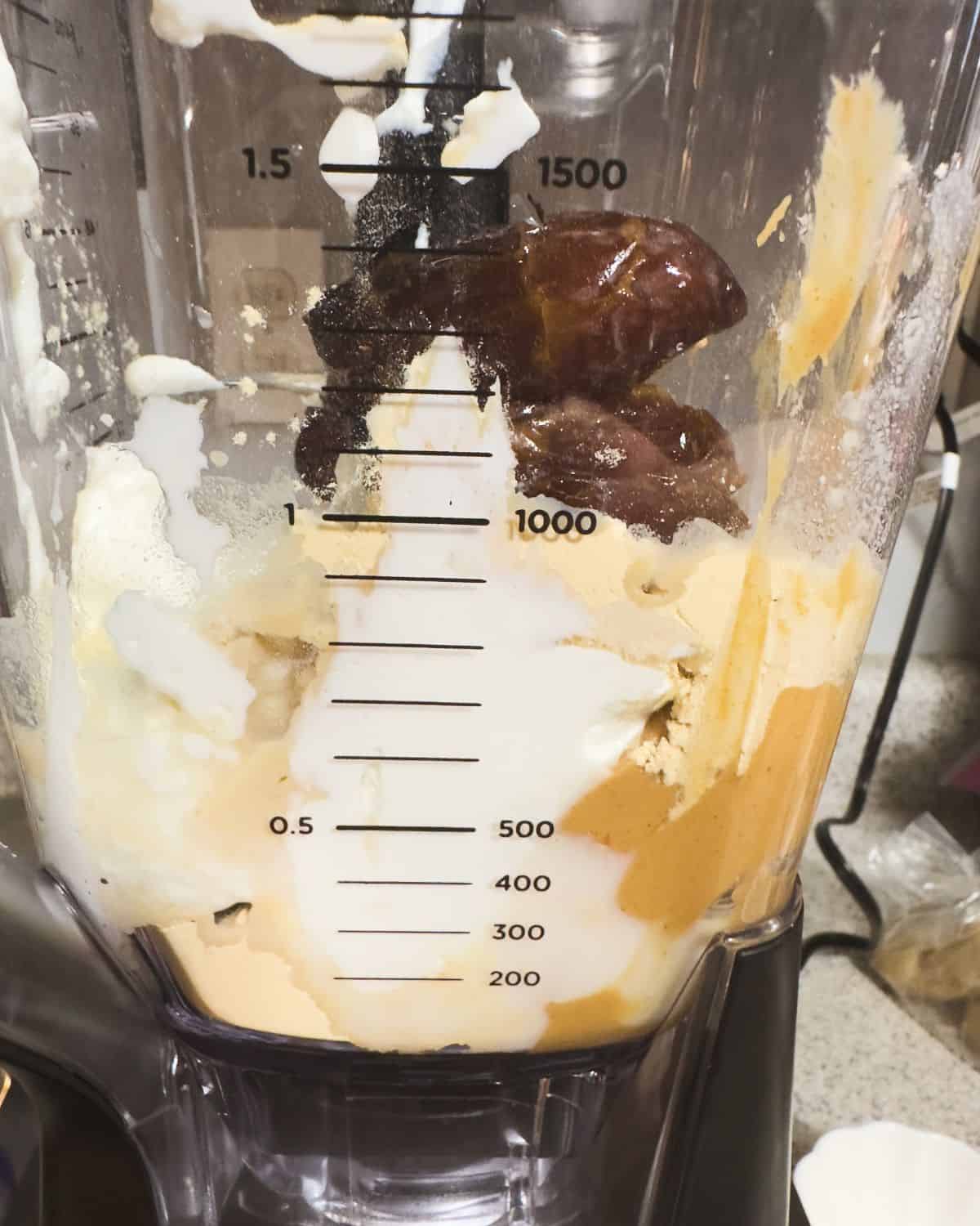 A blender filled with the ingredients for a peanut butter paradise smoothie including Medjool dates and a creamy mixture, awaiting blending.
