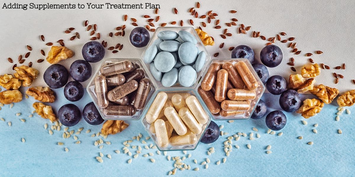 A variety of capsules and tablets in clear containers surrounded by blueberries and nuts on a pale background, illustrating a blend of natural foods and supplements.