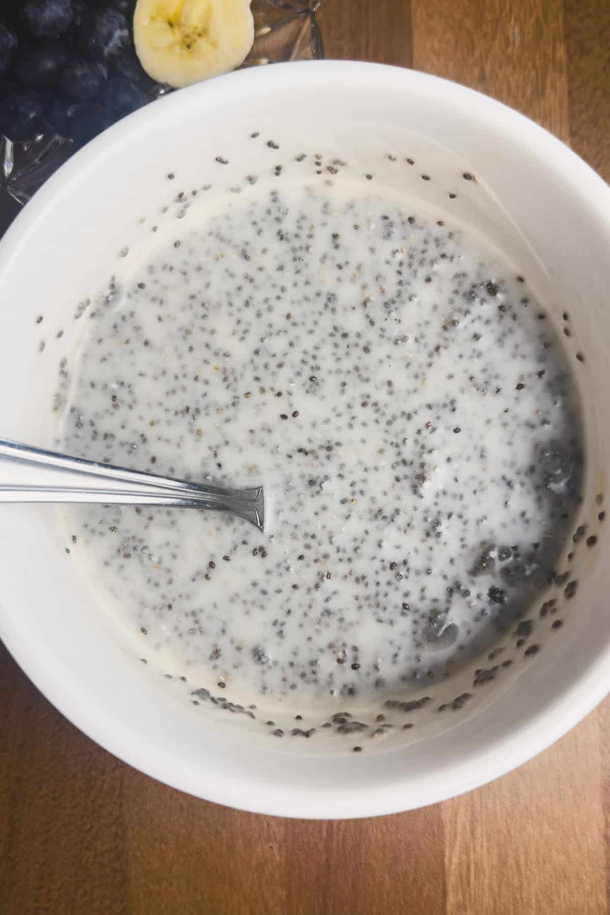 A top-down view of a white bowl filled with chia seed mixture, consisting of milk, chia seeds, maple syrup, and a hint of vanilla, ready to be stirred.